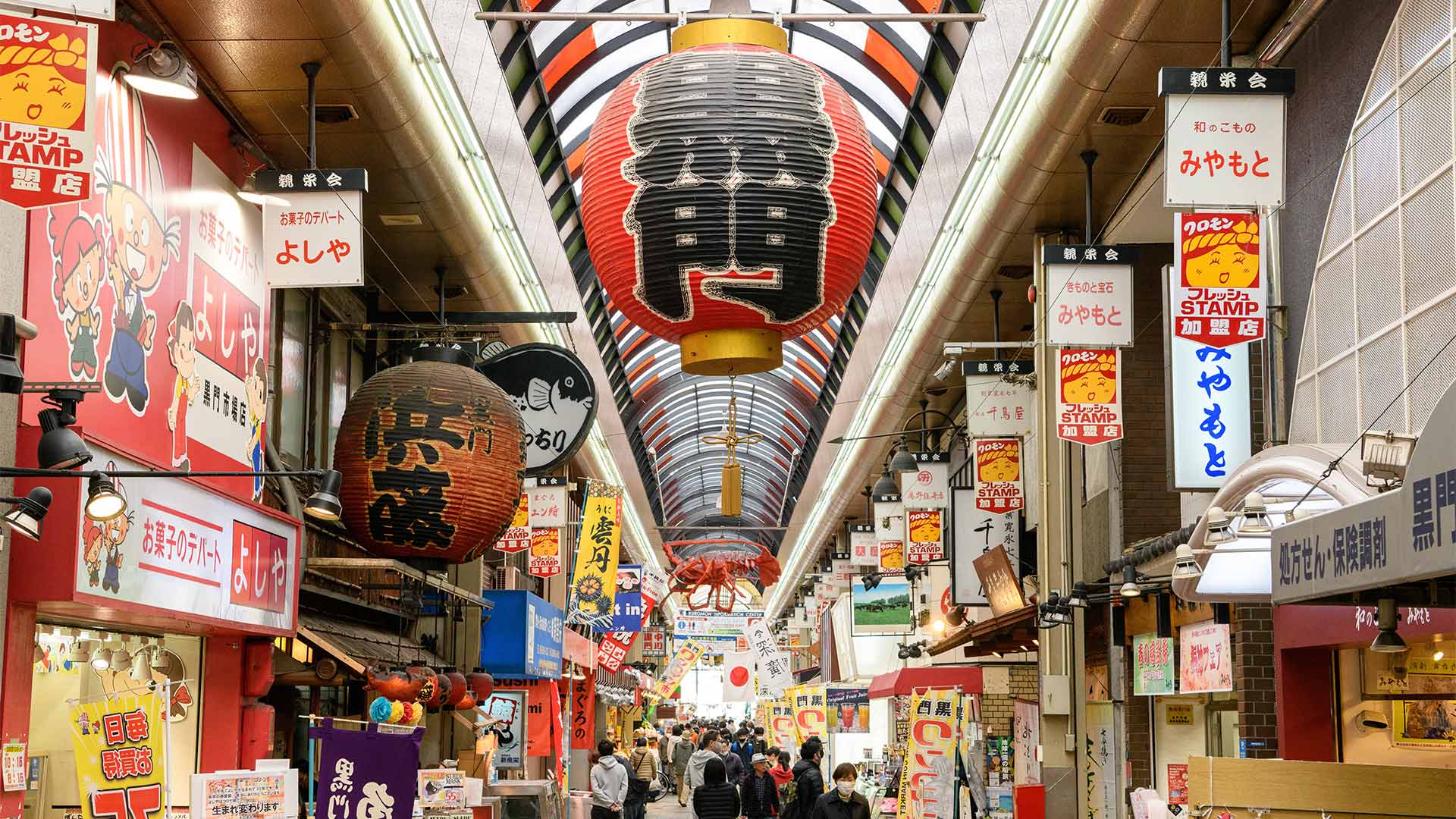 Image of store banners along Kuromon Market with a large paper lantern in the middle.