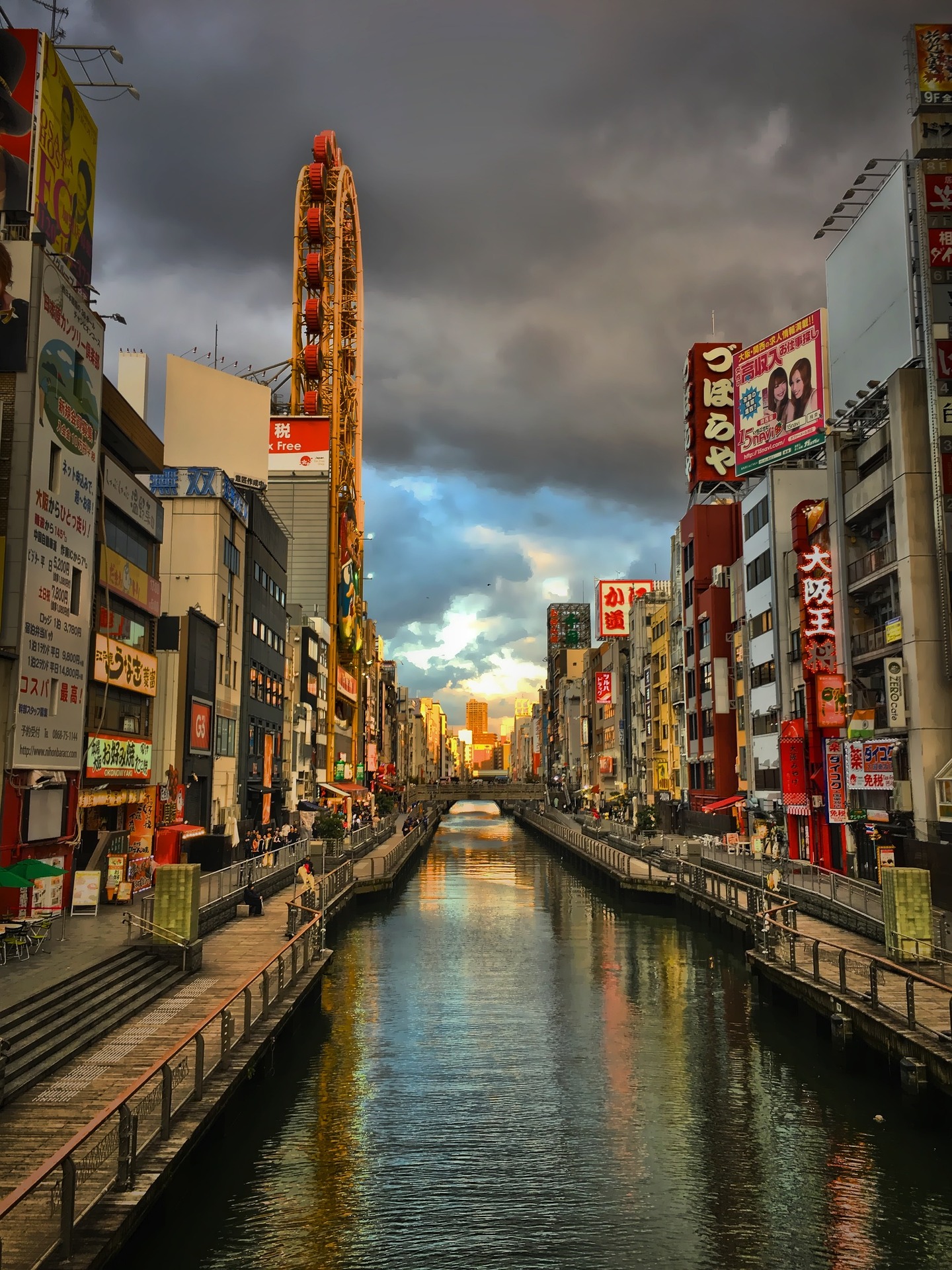 An image of the sun setting on Dotonbori, street signs line buildings parted by a river in the middle of the photo.