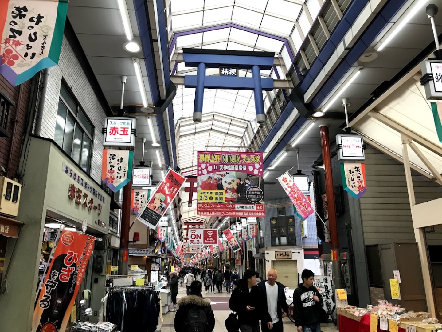Image of people walking through the shopping street with many store banners strung overhead.